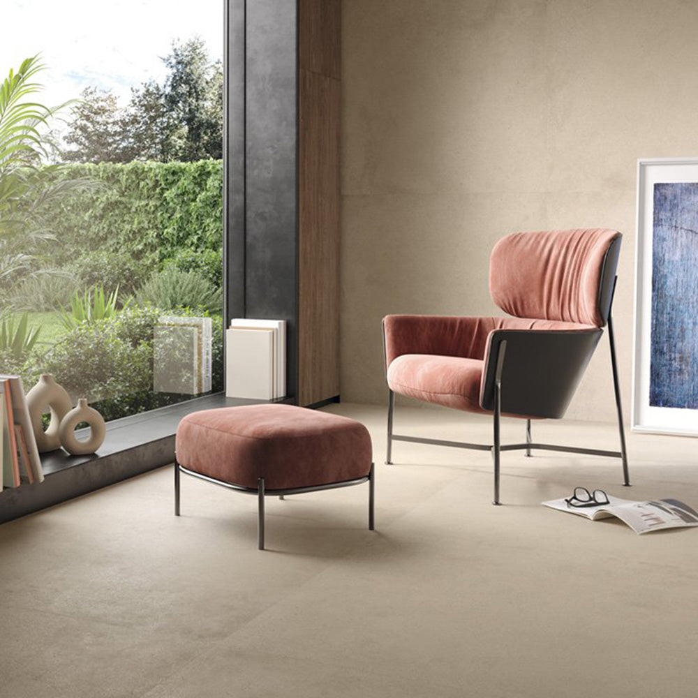 Contemporary living space featuring Riminy Sand Concrete Effect wall and floor tiles 60 × 60cm, showcasing warm sand-toned concrete styling with a soft matt finish, subtle tonal movement, and a calm minimalist aesthetic paired with blush pink seating and natural light.
