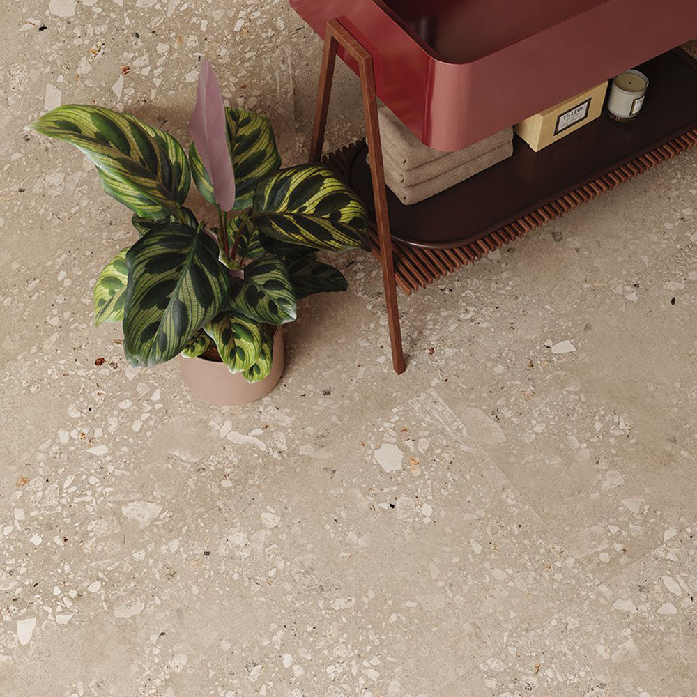Bathroom interior featuring Riminy Sand Cosmo Stone wall and floor tiles 60 × 120cm, showcasing a warm terrazzo-effect surface with natural stone fragments, soft sand tones, and subtle variation, paired with rich wood furniture and indoor greenery for a contemporary organic feel.