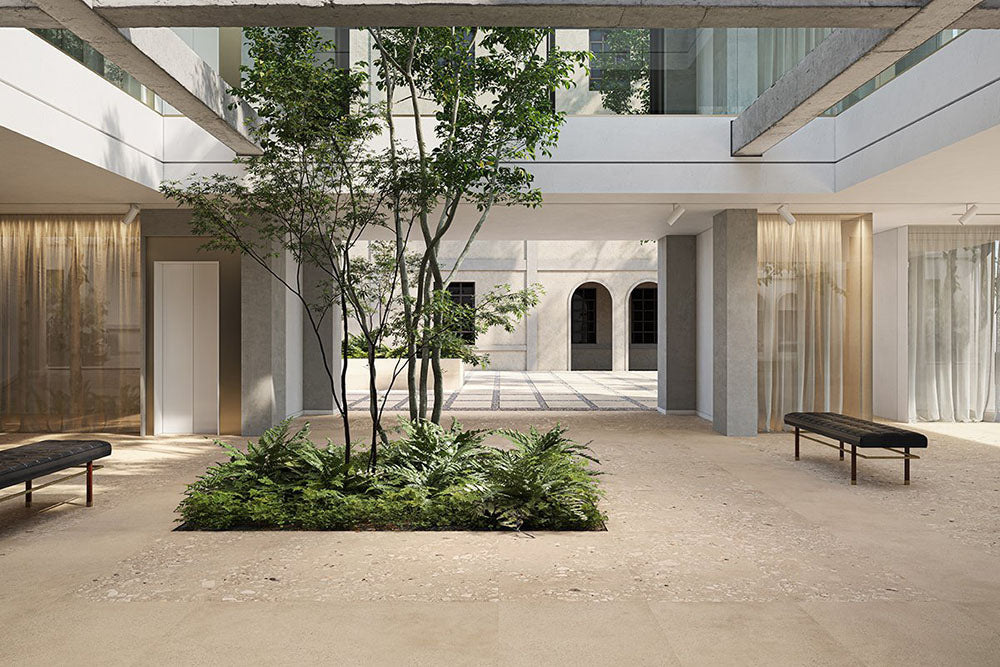 Architectural courtyard featuring Riminy Sand Cosmo Stone wall and floor tiles 60 × 120cm, combining warm sand-toned concrete styling with terrazzo-inspired stone fragments and subtle tonal movement, creating a calm contemporary setting with indoor greenery and minimalist architecture.