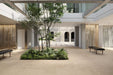 Architectural courtyard featuring Riminy Sand Cosmo Stone wall and floor tiles 60 × 120cm, combining warm sand-toned concrete styling with terrazzo-inspired stone fragments and subtle tonal movement, creating a calm contemporary setting with indoor greenery and minimalist architecture.