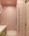 Bathroom interior featuring Rippled Brick Base Stony Pink 5 × 20cm matt ceramic wall tiles, laid vertically with fine linear detail, paired with a glass shower enclosure, terrazzo-effect flooring, and a playful, colour-led vanity area.