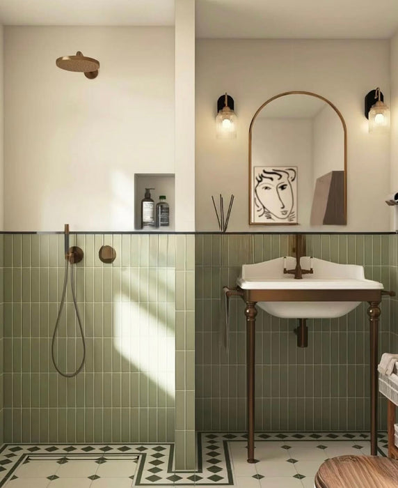 Bathroom featuring Rippled Brick Base Tansy Green Matt 5cm x 20cm wall tiles, laid vertically around the shower and basin, paired with patterned floor tiles, bronze fixtures and an arched mirror.