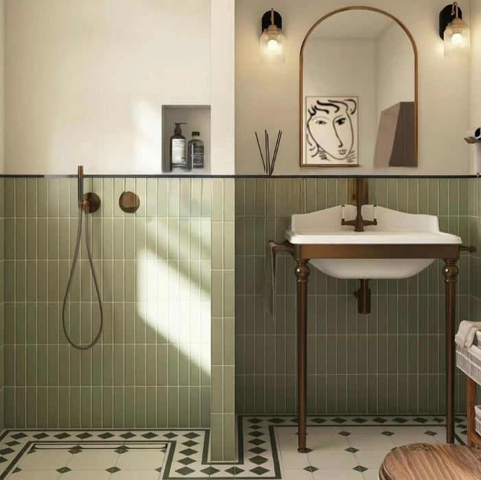 Bathroom featuring Rippled Brick Base Tansy Green Matt 5cm x 20cm wall tiles, laid vertically around the shower and basin, paired with patterned floor tiles, bronze fixtures and an arched mirror.