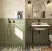 Bathroom featuring Rippled Brick Base Tansy Green Matt 5cm x 20cm wall tiles, laid vertically around the shower and basin, paired with patterned floor tiles, bronze fixtures and an arched mirror.