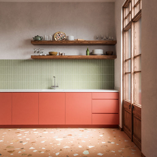 Kitchen featuring Rippled Brick 3D DECOR Tansy Green Matt 5cm x 20cm wall tiles, showcasing a fluted texture and soft green tone, paired with coral cabinetry, terrazzo-style flooring and warm wood details.