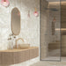 Bathroom interior featuring Contract Pebble Rock Avorio 60x120cm terrazzo effect porcelain wall and floor tiles, paired with a floating vanity, ribbed wood detail, walk-in shower, and brushed brass fittings for a warm, contemporary finish.