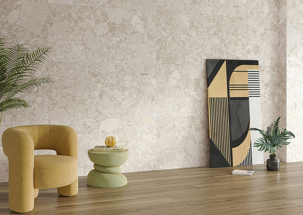 Living room interior featuring Contract Pebble Rock Avorio 60x120cm terrazzo effect porcelain wall tiles, styled with a mustard armchair, wooden flooring, abstract artwork, and greenery for a warm, contemporary finish.