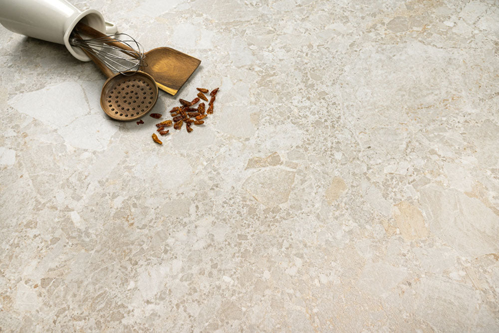 Kitchen surface featuring Contract Pebble Rock Avorio 60x120cm terrazzo effect porcelain tiles, styled with brass utensils, a ceramic container, and warm neutral tones highlighting the natural stone-inspired variation.