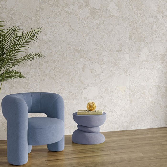 Living room interior featuring Contract Pebble Rock Blanca 60x120cm terrazzo effect porcelain wall tiles, styled with a blue accent chair, wooden flooring, a sculptural side table, and greenery for a soft, contemporary finish.