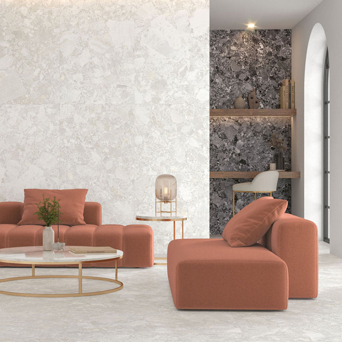 Living room interior featuring Contract Pebble Rock Blanca 60x120cm terrazzo effect porcelain floor and wall tiles, paired with soft coral seating, a round coffee table, and dark terrazzo feature shelving for a contemporary, design-led space.