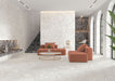 Living room interior featuring Contract Pebble Rock Blanca 60x120cm terrazzo effect porcelain floor and wall tiles, paired with soft coral seating, a round coffee table, and dark terrazzo feature shelving for a contemporary, design-led space.