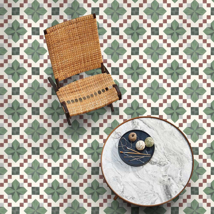 Top-down interior view featuring Geometry Green Clover 20x20cm patterned floor tiles in green, white and soft red tones, styled with a woven chair and marble table in a relaxed, contemporary living space.