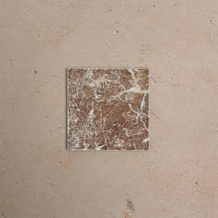 Single Fitzrovia Rosso 15.2x15.2cm tumbled natural marble tile displayed on a warm neutral surface, showcasing rich terracotta tones, natural veining, and a softly aged, textured finish.