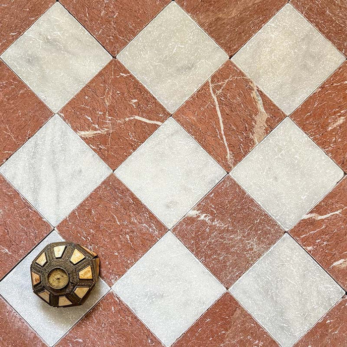 Flat lay of Fitzrovia Rosso 15.2x15.2cm tumbled natural marble tiles paired with Fitzrovia White in a classic chequerboard pattern, showcasing warm terracotta tones, soft white contrast, natural veining, and a decorative accent piece.