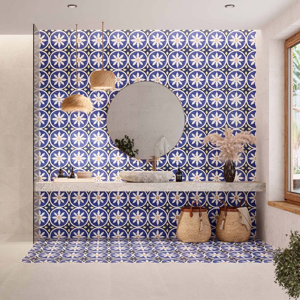 Bathroom featuring Santillana Blue and Yellow patterned wall and floor tiles, showcasing a bold Mediterranean-inspired floral geometric design in vibrant cobalt blue, warm yellow and crisp white tones, paired with a floating stone vanity, round mirror, woven pendant lights, natural baskets and soft neutral finishes for a bright, characterful interior.