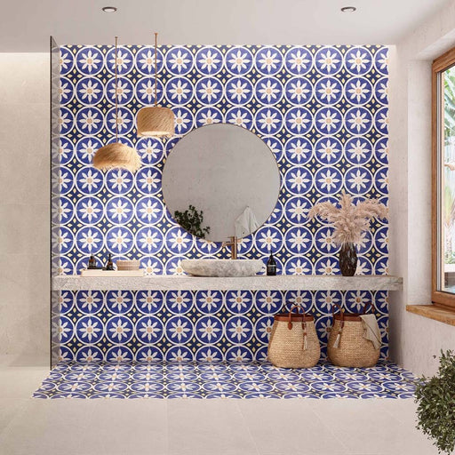 Bathroom featuring Santillana Blue and Yellow patterned wall and floor tiles, showcasing a bold Mediterranean-inspired floral geometric design in vibrant cobalt blue, warm yellow and crisp white tones, paired with a floating stone vanity, round mirror, woven pendant lights, natural baskets and soft neutral finishes for a bright, characterful interior.