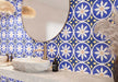 Bathroom featuring Santillana Blue and Yellow patterned wall and floor tiles, showcasing a bold Mediterranean-inspired floral geometric design in vibrant cobalt blue, warm yellow and crisp white tones, paired with a floating stone vanity, round mirror, woven pendant lights, natural baskets and soft neutral finishes for a bright, characterful interior.