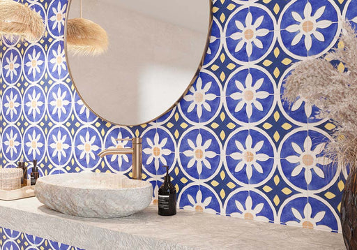 Bathroom featuring Santillana Blue and Yellow patterned wall and floor tiles, showcasing a bold Mediterranean-inspired floral geometric design in vibrant cobalt blue, warm yellow and crisp white tones, paired with a floating stone vanity, round mirror, woven pendant lights, natural baskets and soft neutral finishes for a bright, characterful interior.
