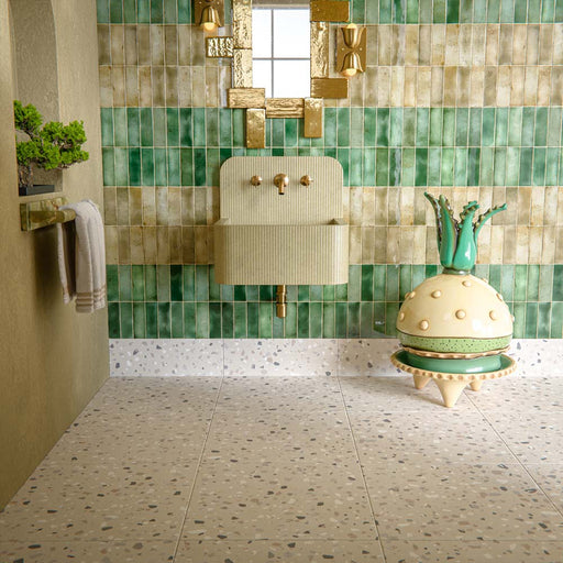 Bathroom interior featuring Veneto Medium Sand 60x60cm terrazzo effect porcelain floor tiles, paired with green brick wall tiles, brass fixtures and a sculptural basin for a warm, design-led finish.
