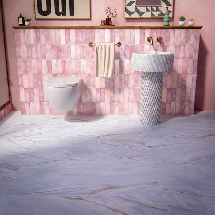 Bathroom setting featuring Bassano River Blue 60x120cm matt porcelain wall and floor tiles, showcasing soft blue-grey tones with subtle veining, paired with coral pink brick wall tiles, brass fittings and a fluted marble basin.