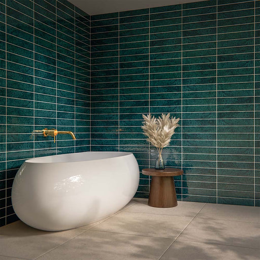Bathroom interior featuring Malaga Amun Blue Brick gloss wall tiles in 6.5x32.8cm format, installed horizontally around a freestanding bath, showcasing rich blue tonal variation with brushed brass tap and neutral floor tiles.