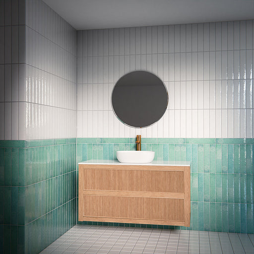 Bathroom interior featuring Malaga Aqua Brick gloss wall tiles in 6.5x32.8cm format, installed vertically as a half-height feature beneath white tiles, styled with a floating wood vanity, round mirror and brass tap.