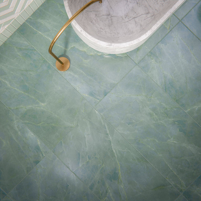 Bathroom setting featuring Bassano Sea Green 60x120cm porcelain wall and floor tiles with a subtle marble effect, showcasing soft blue-green tones and gentle veining, paired with a freestanding bath and brushed brass fixtures for a calm, spa-like feel.