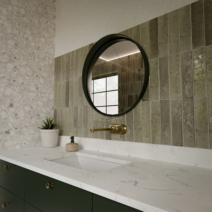 Izmir Sage Green 6x25cm gloss brick tiles used throughout a contemporary walk-in shower, showcasing soft sage tones with natural variation and a reflective glazed finish. The elongated format enhances vertical lines, adding texture and depth, while pairing beautifully with terrazzo-style walls, brass fittings and patterned floor tiles for a cohesive, design-led bathroom space.