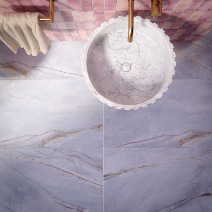 Bathroom setting featuring Bassano River Blue 60x120cm matt porcelain wall and floor tiles, showcasing soft blue-grey tones with subtle veining, paired with coral pink brick wall tiles, brass fittings and a fluted marble basin.