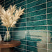 Bathroom interior featuring Malaga Amun Blue Brick gloss wall tiles in 6.5x32.8cm format, installed horizontally around a freestanding bath, showcasing rich blue tonal variation with brushed brass tap and neutral floor tiles.