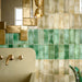 Bathroom interior featuring Fusion Bricks moss and jade green 6.5x20cm ceramic wall tiles in a horizontal layout, styled with a sculptural sink, brass fixtures, terrazzo floor and decorative accents.