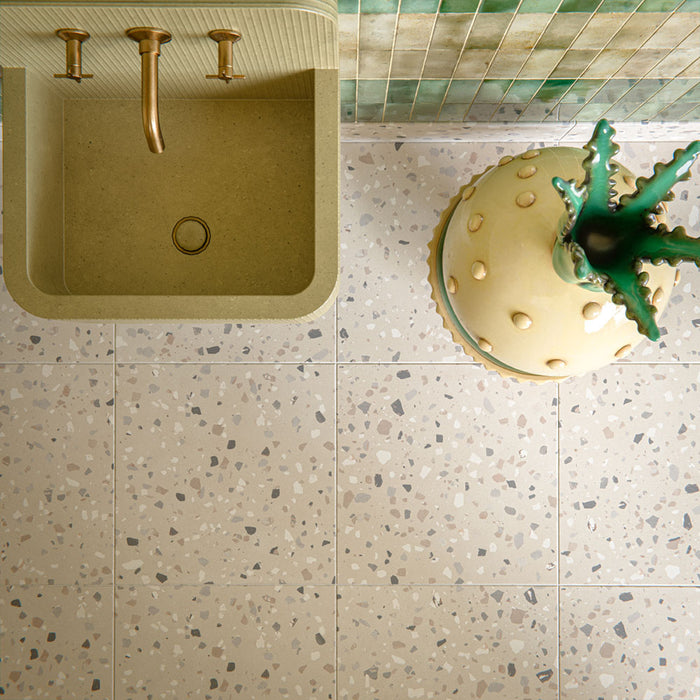 Bathroom interior featuring Veneto Medium Sand 60x60cm terrazzo effect porcelain floor tiles, paired with green brick wall tiles, brass fixtures and a sculptural basin for a warm, design-led finish.