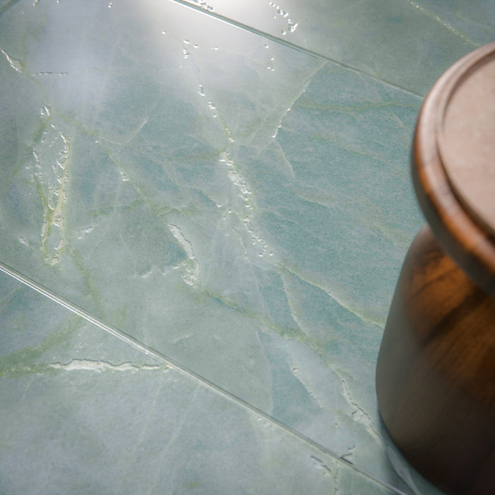 Bathroom setting featuring Bassano Sea Green 60x120cm porcelain wall and floor tiles with a subtle marble effect, showcasing soft blue-green tones and gentle veining, paired with a freestanding bath and brushed brass fixtures for a calm, spa-like feel.