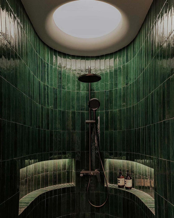 Curved shower area featuring Mizu green porcelain wall and floor tiles in a 6 × 24cm format, laid vertically to create a rich, glossy backdrop, complemented by built-in shelving and dark metal shower fittings.