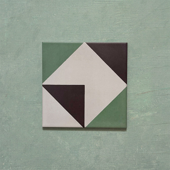 Single Geometry Angles Patterned Tile in 20cm x 20cm, featuring a modern geometric design with green, white, and black triangular shapes arranged to form a diamond motif, displayed on a textured green background.