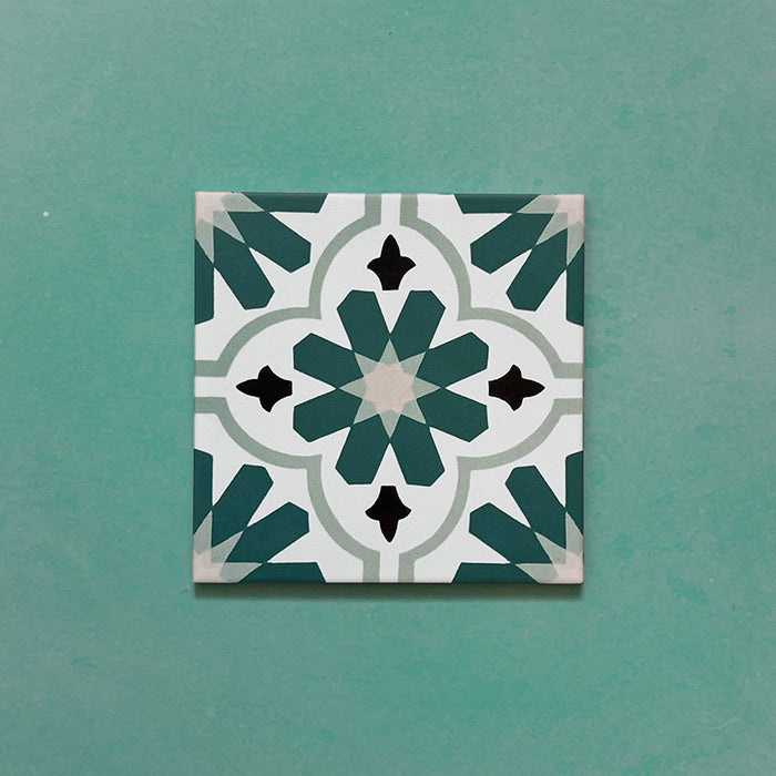 Flatlay featuring a single Clarence House Teal Green 20x20cm Victorian Moroccan-style porcelain tile, showcasing a detailed geometric floral pattern in teal, white, and black on a green background.