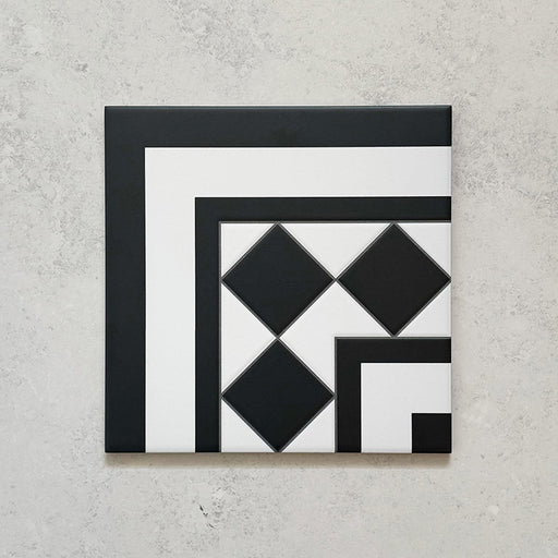 Single Sloane Square Black 25x25cm Victorian-style ceramic corner tile featuring a black and white geometric border and diamond pattern, shown against a light grey textured background in a product close-up.