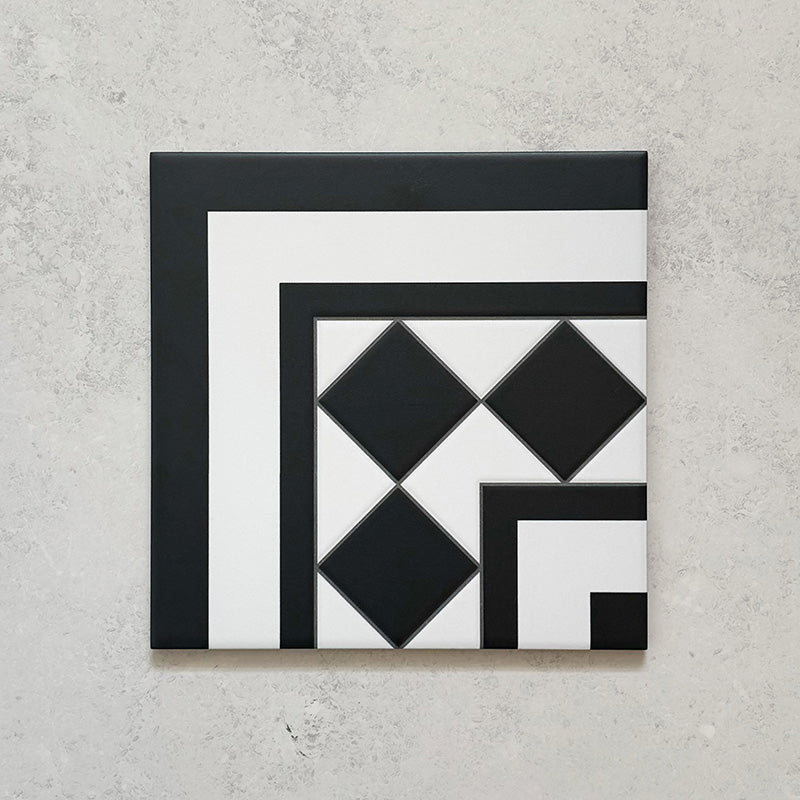 Single Sloane Square Black 25x25cm Victorian-style ceramic corner tile featuring a black and white geometric border and diamond pattern, shown against a light grey textured background in a product close-up.