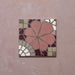 Single Bloom Rose Pink 20x20cm Moroccan-style ceramic tile featuring a floral pattern in blush pink, burgundy, taupe, and white tones, shown against a pink textured background in a close-up view.