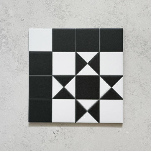 Single Sloane Square 25x25cm Victorian-style ceramic tile featuring a classic black and white geometric star pattern, shown against a light grey textured background in a close-up view.