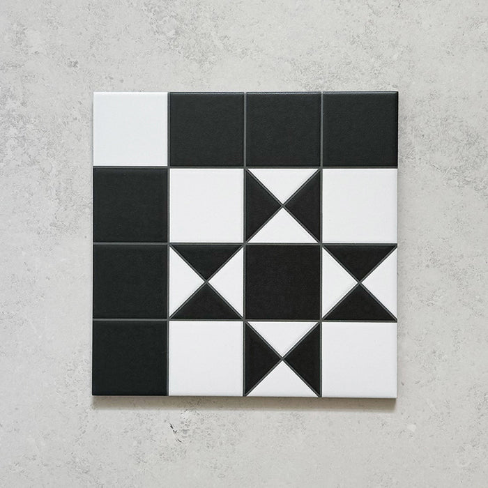 Single Sloane Square 25x25cm Victorian-style ceramic tile featuring a classic black and white geometric star pattern, shown against a light grey textured background in a close-up view.