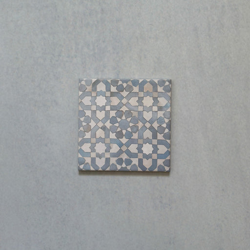 Single Bedouin Tetuan Blue Moroccan-style ceramic tile, 15x15cm, showcasing an intricate geometric star and cross pattern in soft blue, white, and taupe tones with a handcrafted finish on a pale textured background.