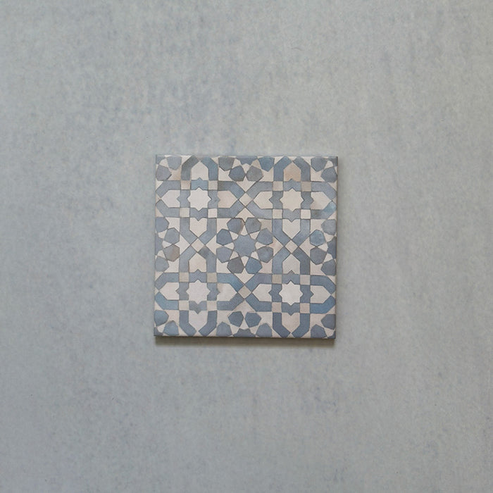 Single Bedouin Tetuan Blue Moroccan-style ceramic tile, 15x15cm, showcasing an intricate geometric star and cross pattern in soft blue, white, and taupe tones with a handcrafted finish on a pale textured background.