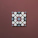 Close-up of Agraba Mini Atlas 15x15cm Moroccan-style ceramic tile featuring a geometric star pattern in blue, terracotta, black, and white tones on a warm burgundy background.