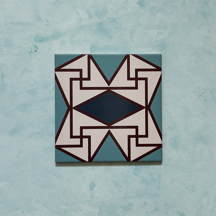 Single tile image showing the Geometry Iris 20x20cm patterned tile with a detailed geometric motif in teal, navy, terracotta-red, and cream, photographed against a soft mottled aqua background.