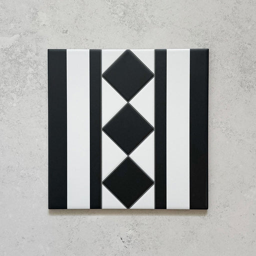 Single Sloane Square Black 25x25cm Victorian-style ceramic border tile featuring a black and white geometric stripe and diamond pattern, shown against a light grey textured background in a product close-up.