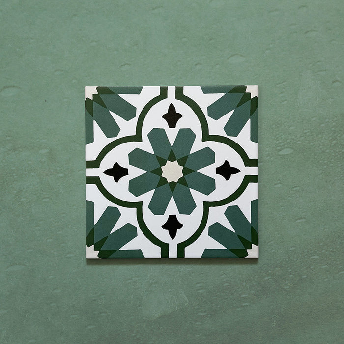 Flatlay featuring a single Clarence House Verde Green 20x20cm Victorian Moroccan-style porcelain tile, showcasing an intricate green and white geometric floral pattern on a textured green background.