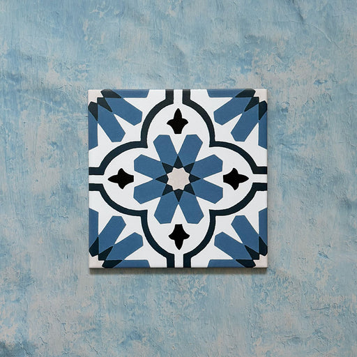 Flatlay featuring a single Clarence House Azul Blue 20x20cm Victorian Moroccan-style porcelain tile, showcasing an intricate blue and white floral geometric pattern on a textured blue background.