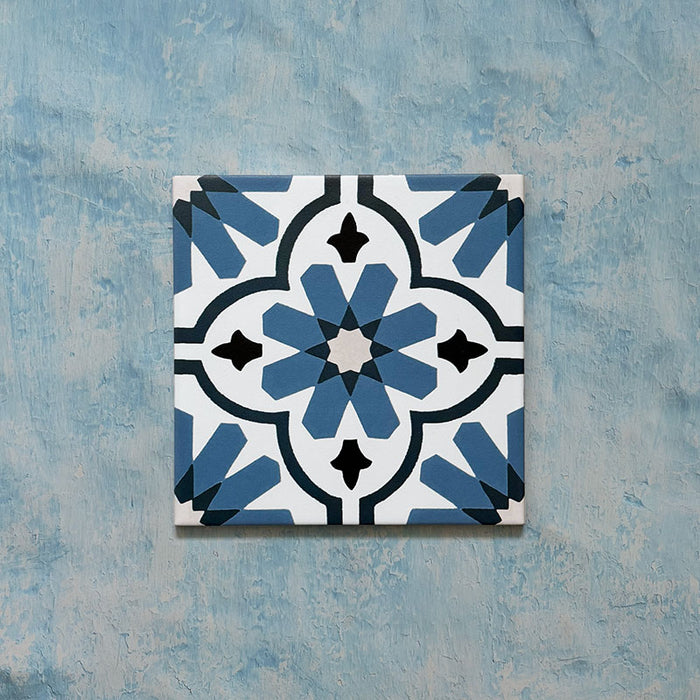 Flatlay featuring a single Clarence House Azul Blue 20x20cm Victorian Moroccan-style porcelain tile, showcasing an intricate blue and white floral geometric pattern on a textured blue background.