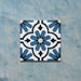 Flatlay featuring a single Clarence House Azul Blue 20x20cm Victorian Moroccan-style porcelain tile, showcasing an intricate blue and white floral geometric pattern on a textured blue background.
